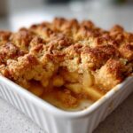Close-up of a golden brown baked Apple Crisp with a crumbly topping in a white ceramic dish.