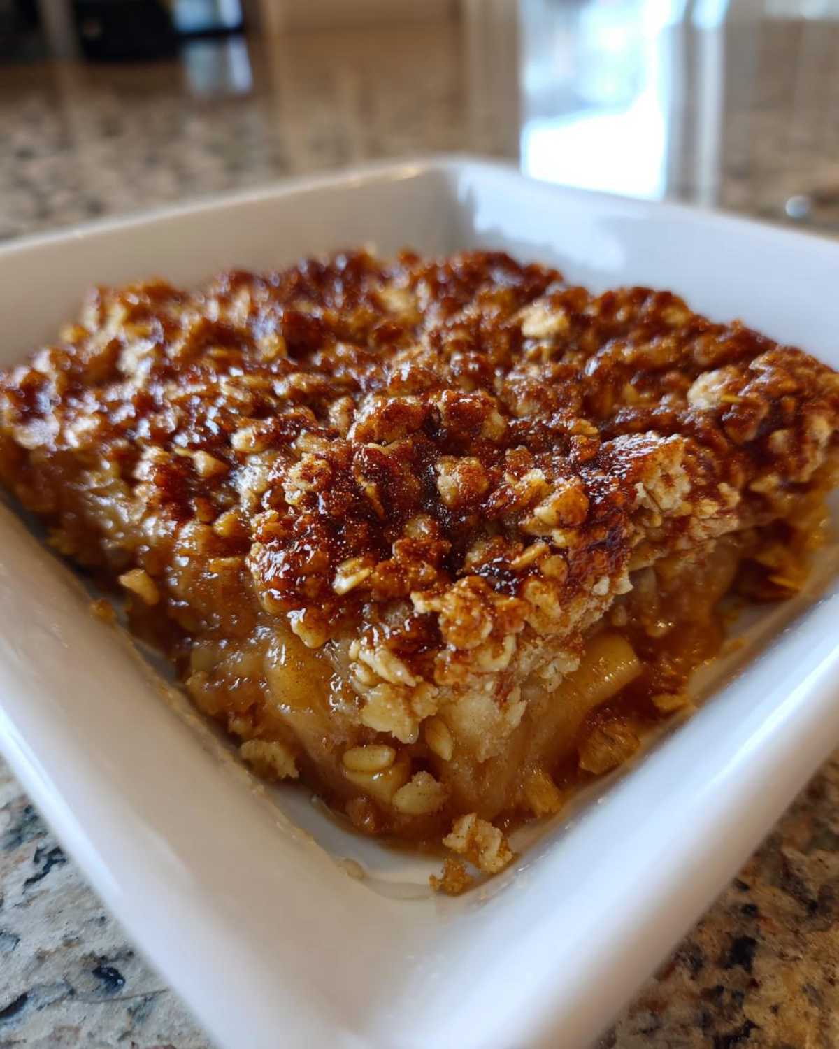 A close-up view of a square serving of baked Apple Crisp with a golden brown, crunchy oat topping and soft apple filling.