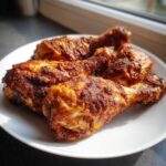 Four crispy, well-seasoned Baked Chicken Legs resting on a white plate, highlighted by natural sunlight.