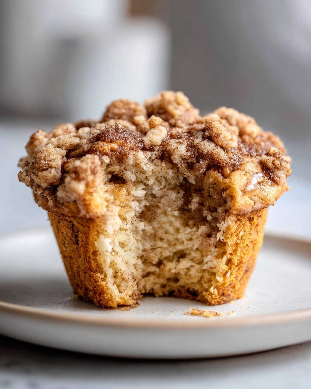 Close-up of an Apple Cinnamon Crumb Muffin with a bite taken out, showing the moist interior and thick cinnamon streusel topping.