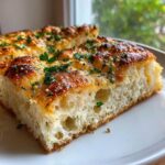 A thick slice of fluffy Garlic Parmesan Focaccia Bread with a golden, cheesy crust and fresh parsley.