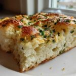 A thick slice of fluffy Garlic Parmesan Focaccia Bread topped with melted cheese and fresh parsley.