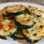 Close-up of several slices of Garlic Parmesan Zucchini Roast, topped with melted, browned cheese and herbs.