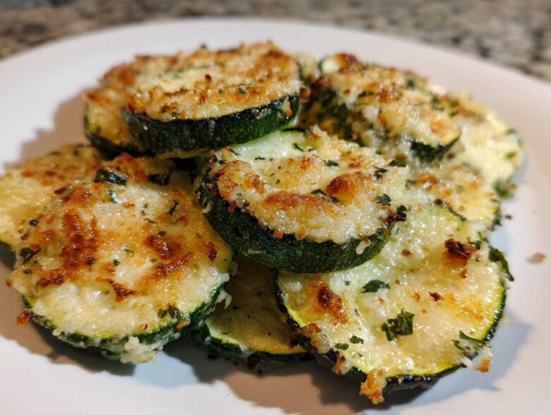 Close-up of several slices of Garlic Parmesan Zucchini Roast, topped with melted, browned cheese and herbs.