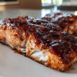 A close-up of a flaky salmon fillet generously coated in a dark, sticky Gochujang Honey Glazed Salmon sauce.