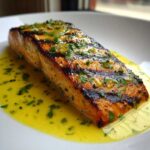Close-up of a perfectly grilled salmon fillet topped with bright lemon butter sauce and fresh parsley.
