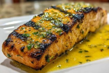 Close-up of a perfectly grilled salmon fillet generously topped with lemon butter sauce and fresh herbs.