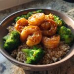 A close-up of a bowl filled with brown rice, bright green broccoli florets, and glossy, glazed shrimp, ready to eat as Honey Garlic Shrimp Bowls.