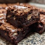 Close-up of two stacked, fudgy Kit Kat Brownie Bars showing a shiny, crackly top and visible pieces of Kit Kat candy inside.