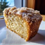 Close-up of a moist slice of Lemon Coffee Cake with Lemon Crumb Topping, drizzled with glaze.