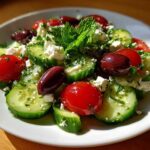 Close-up of a fresh Mediterranean Cucumber Salad featuring sliced cucumbers, cherry tomatoes, Kalamata olives, and feta cheese.