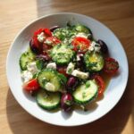 A vibrant plate of Mediterranean Cucumber Salad featuring sliced cucumbers, tomatoes, Kalamata olives, feta cheese, and fresh mint.