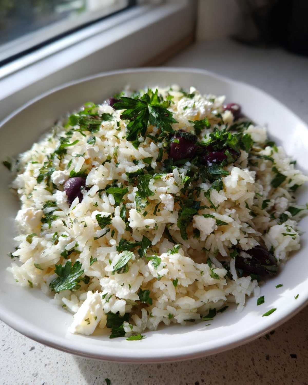 Close-up of a bowl of bright Mediterranean Rice mixed with feta cheese, Kalamata olives, and fresh parsley.