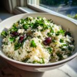 A bowl of vibrant Mediterranean Rice mixed with crumbled feta cheese, chopped parsley, and Kalamata olives.