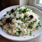 A white bowl filled with fluffy Mediterranean Rice mixed with chopped parsley, feta cheese, and Kalamata olives.