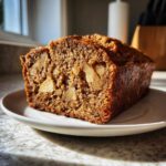 A close-up of a moist Apple Cinnamon Bread loaf, showing large chunks of baked apple inside the rich brown crumb.