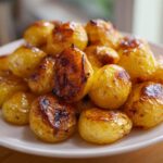 A close-up of golden brown, crispy Oven Roasted Baby Potatoes piled high on a white plate.