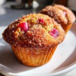A close-up of a golden-brown Rhubarb Muffins with Cinnamon Sugar Topping, featuring visible pink rhubarb pieces.