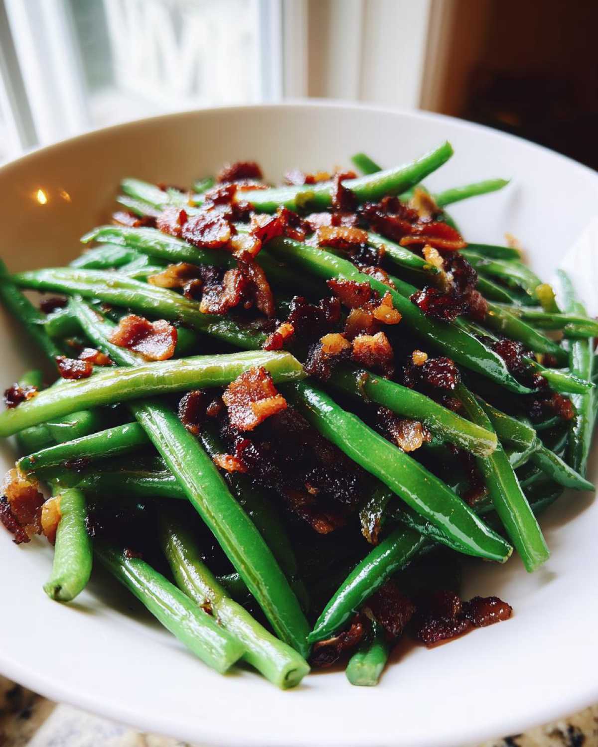 A close-up of bright green Sautéed Green Beans with Crispy Bacon served in a white bowl.