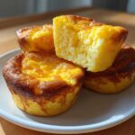 Three golden-brown Starbucks Copycat Egg Bites stacked on a white plate, one cut open to show the fluffy interior.